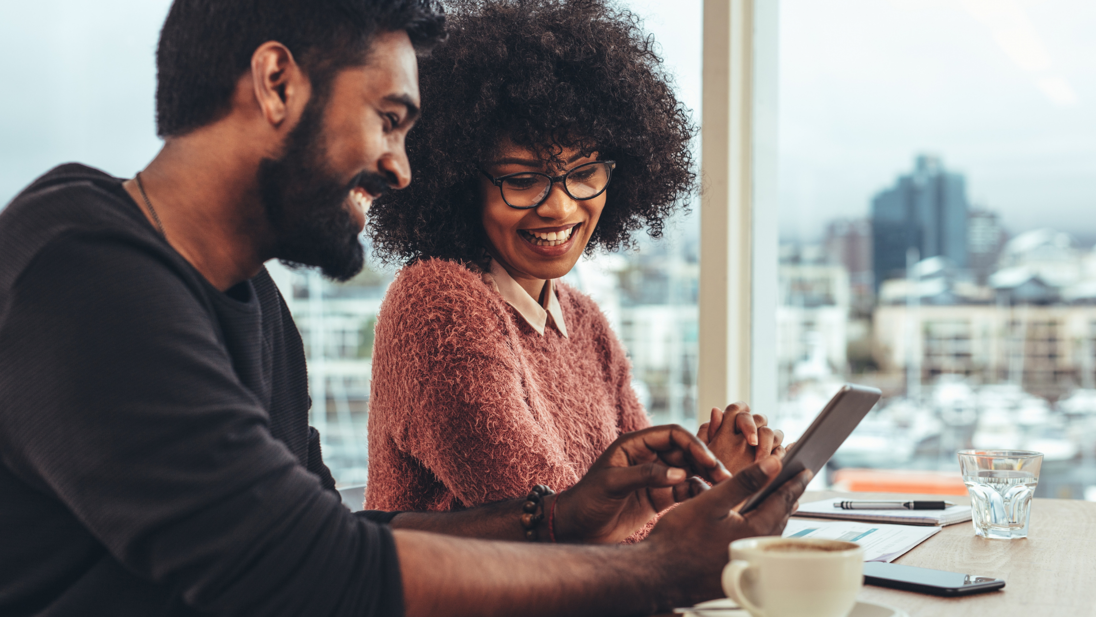 Photo of male showing cell phone screen to female while grabbing a cup of coffee. They're both smiling