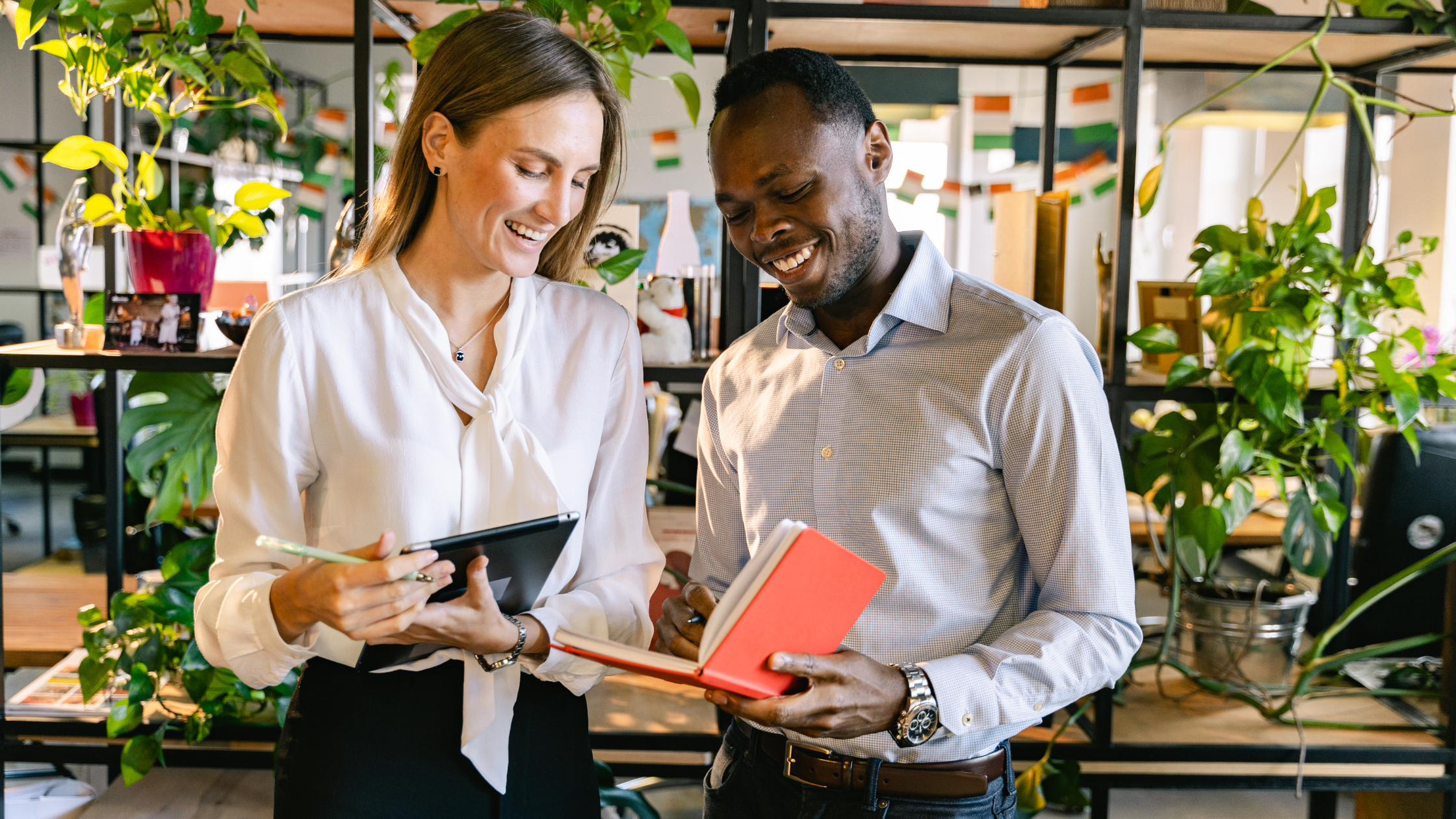 Male coworker points to open notebook while standing next to female coworker 