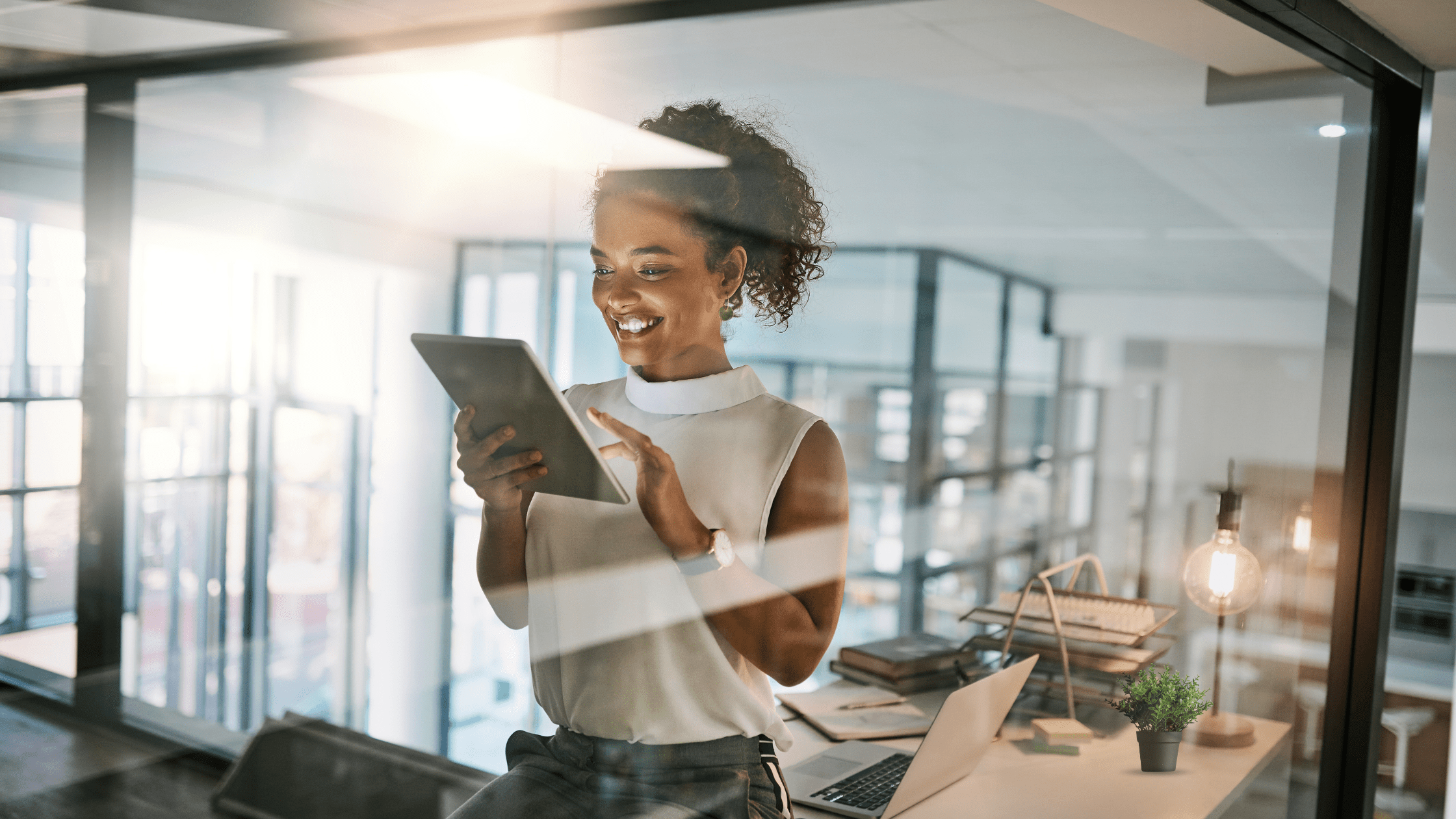 Female standing in her office, pictured behind glass, using a tablet.