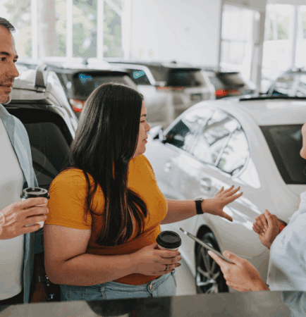Male and female talking to female salesperson in front of vehicle showroom.