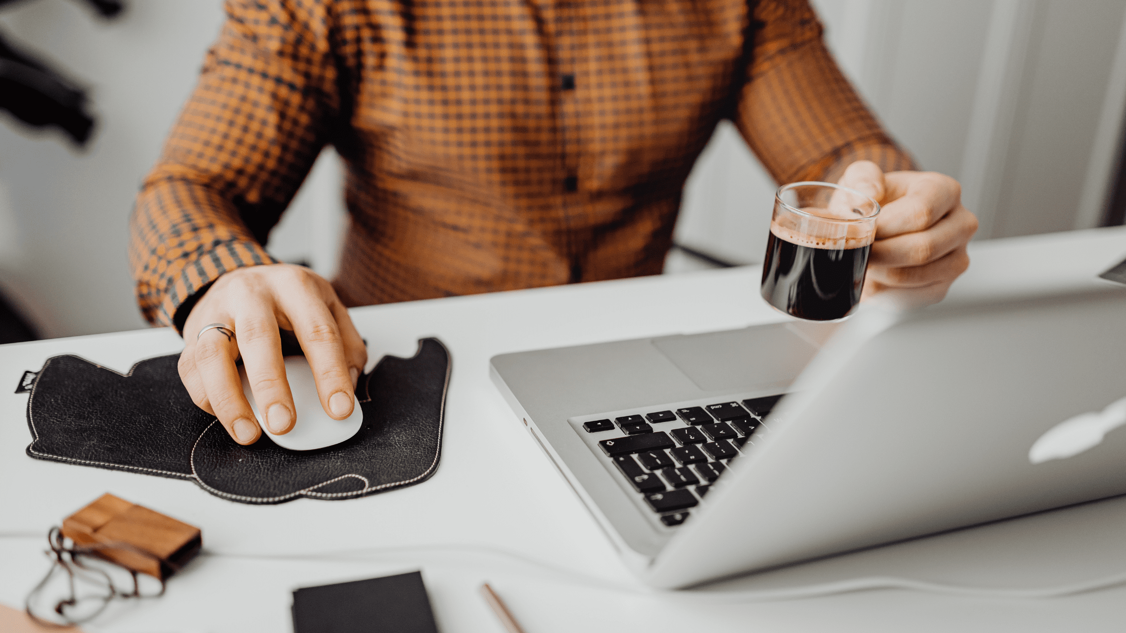 person is holding coffee in their left hand and using the mouse with their right, as they use their laptop